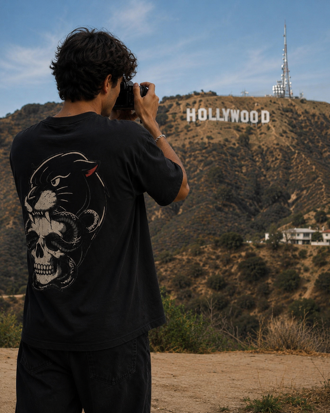 Person taking a photo of the Hollywood sign with FEAR NONE Black t-shirt featuring a skull design.